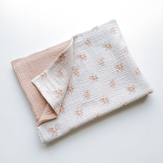 kocyk muślinowy w kolorze różu oraz wzór w różyczki na kremowym tle