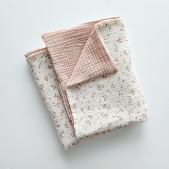 kocyk muślinowy w kolorze różu oraz wzór w kwiatuszki na beżu