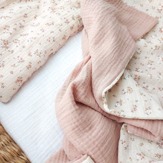 kocyk muślinowy w kolorze różu oraz wzór w kwiatuszki na beżu