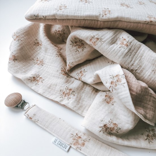 kocyk muślinowy w kolorze różu oraz wzór w różyczki na kremowym tle