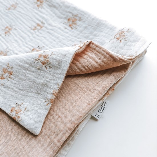 kocyk muślinowy w kolorze różu oraz wzór w różyczki na kremowym tle