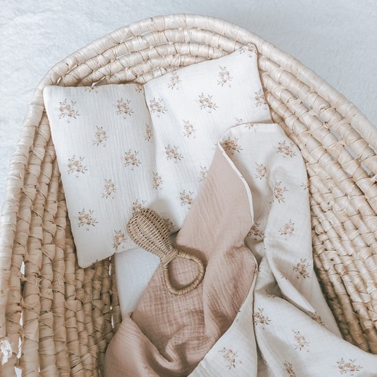 kocyk muślinowy w kolorze różu oraz wzór w różyczki na kremowym tle