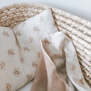 kocyk muślinowy w kolorze różu oraz wzór w różyczki na kremowym tle