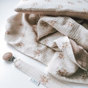kocyk muślinowy w kolorze różu oraz wzór w różyczki na kremowym tle